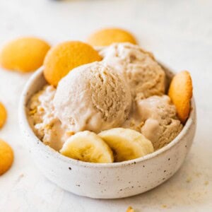 High-protein banana ice cream served in a bowl with banana slices, and vanilla wafers on the side.