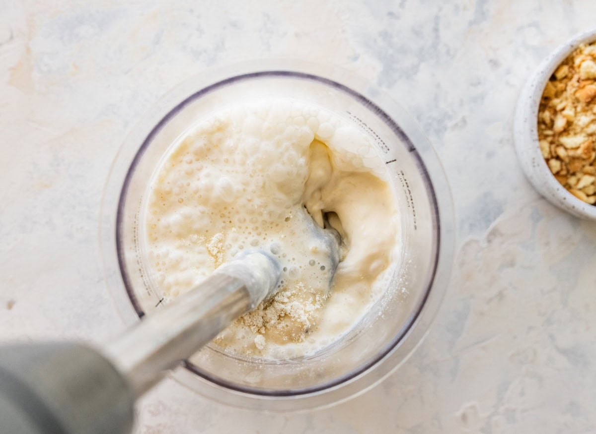 An immersion blender in a container blending banana and protein powder.