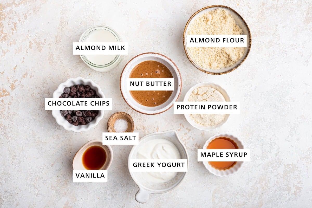 Ingredients measured out to make Protein Cookie Dough: almond flour, vanilla protein powder, maple syrup, almond/cashew/peanut butter, Greek yogurt, almond milk, sea salt, vanilla and chocolate chips.