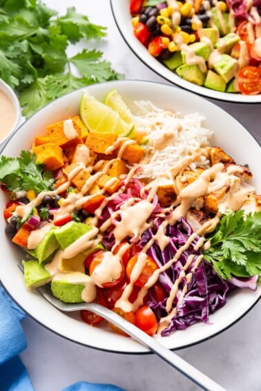 A serving of a BBQ chicken bowl with fresh vegetables and ranch dressing drizzle.