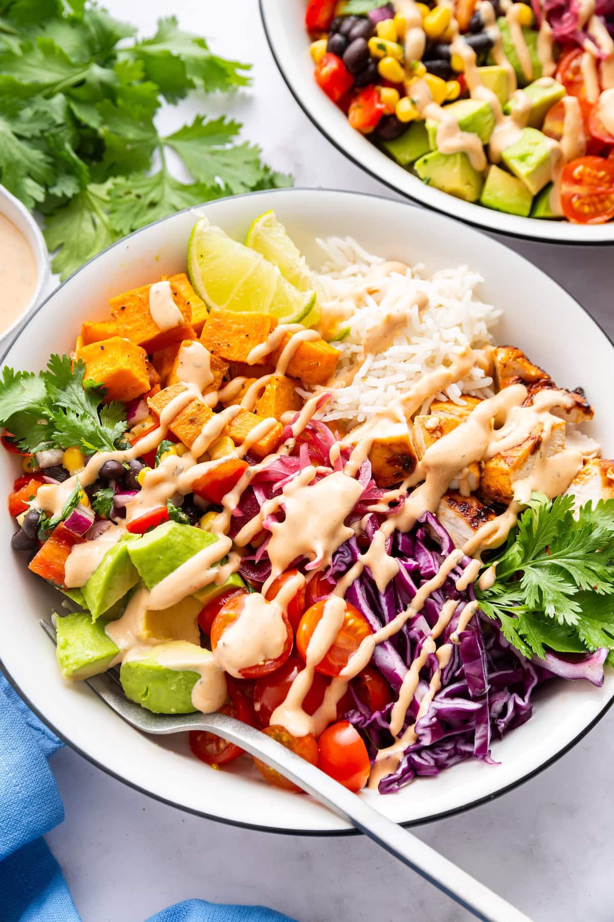 A serving of a BBQ chicken bowl with fresh vegetables and ranch dressing drizzle.