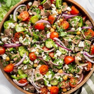 Chimichurri steak salad in a large wooden bowl garnished with feta and cilantro.