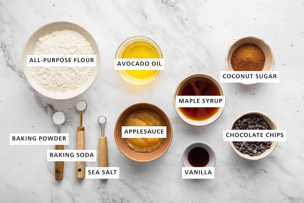 Ingredients measured out for mini chocolate chip muffins: all purpose flour, avocado oil, coconut sugar, maple syrup, applesauce, vanilla, chocolate chips, baking powder, baking soda, and sea salt.