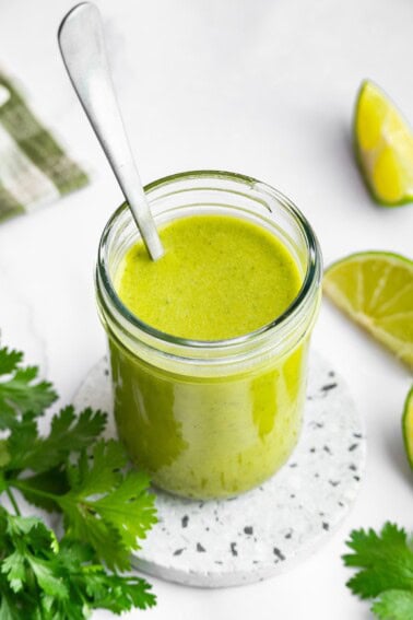 Cilantro lime dressing in a glass mason jar with a metal spoon in the jar of dressing.