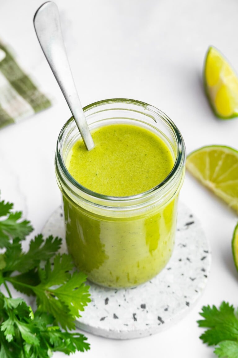 Cilantro lime dressing in a glass mason jar with a metal spoon in the jar of dressing.