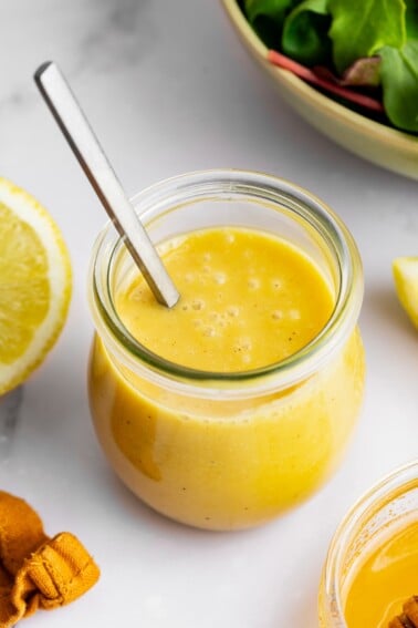 A honey mustard salad dressing in a glass jar with a metal spoon.