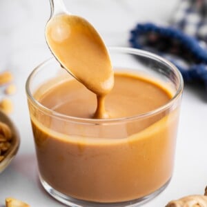 A peanut dressing in a glass cup with a metal spoon being lifted from the cup.