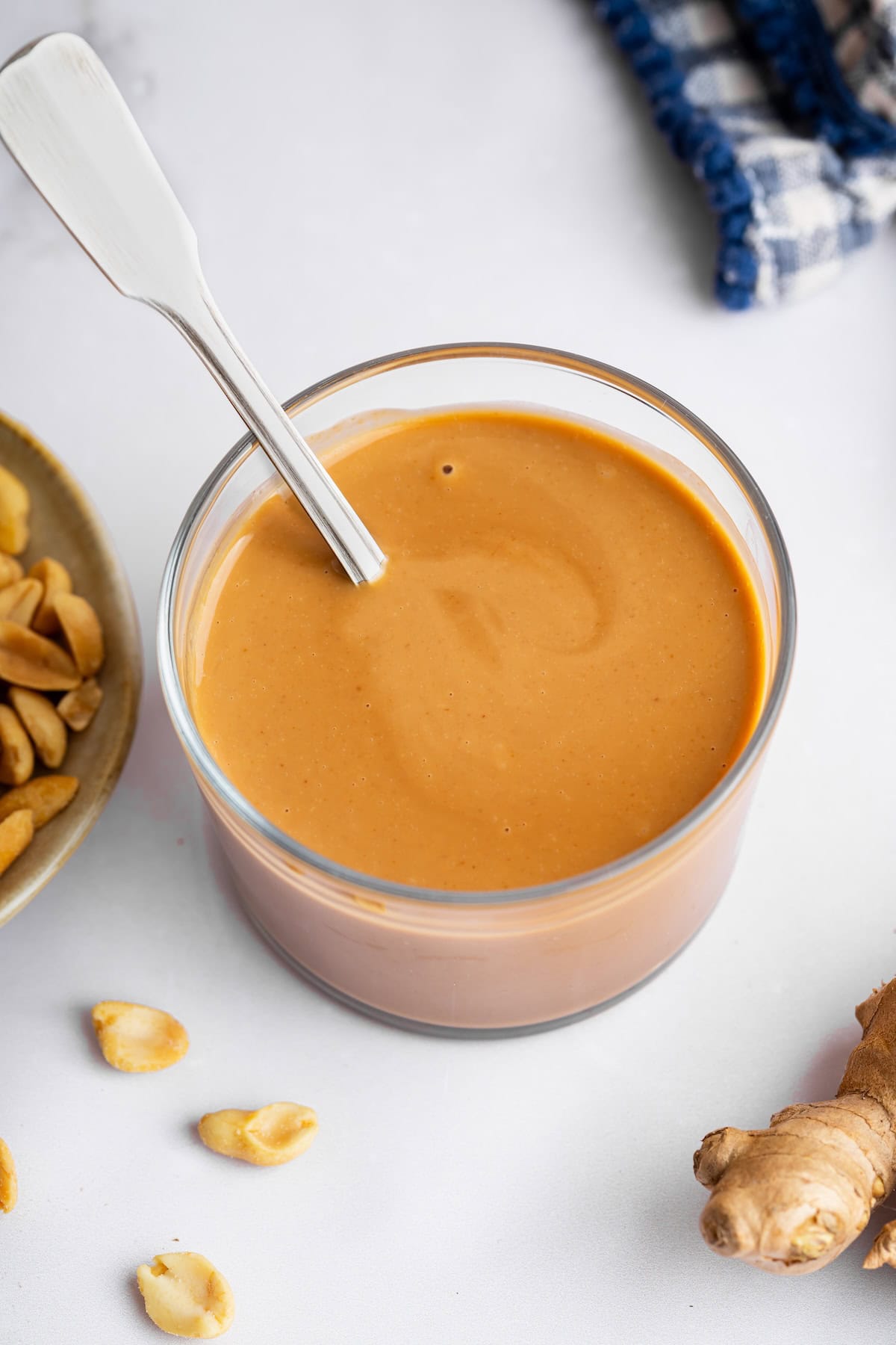 A creamy peanut dressing in a glass cup with peanuts and fresh ginger to the side.