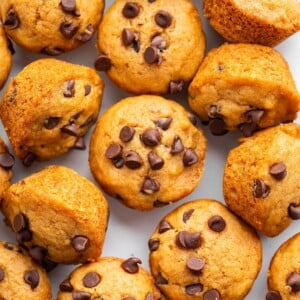 Mini chocolate chip muffins on a table close to one another.