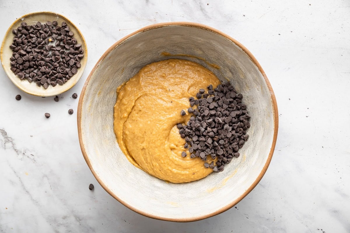 Chocolate chips added to a large mixing bowl with mini muffin batter.