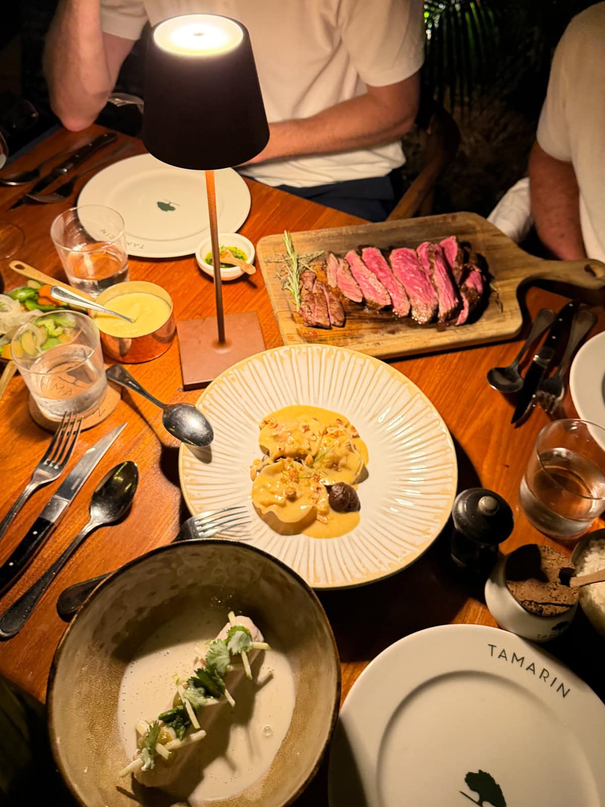 Dinner table spread at Tamarin restaurant with steak on cutting board and pasta dish