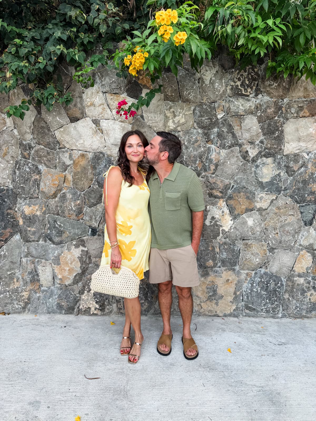 Brittany and Isaac sharing a kiss against a stone wall with tropical flowers in St. Barths