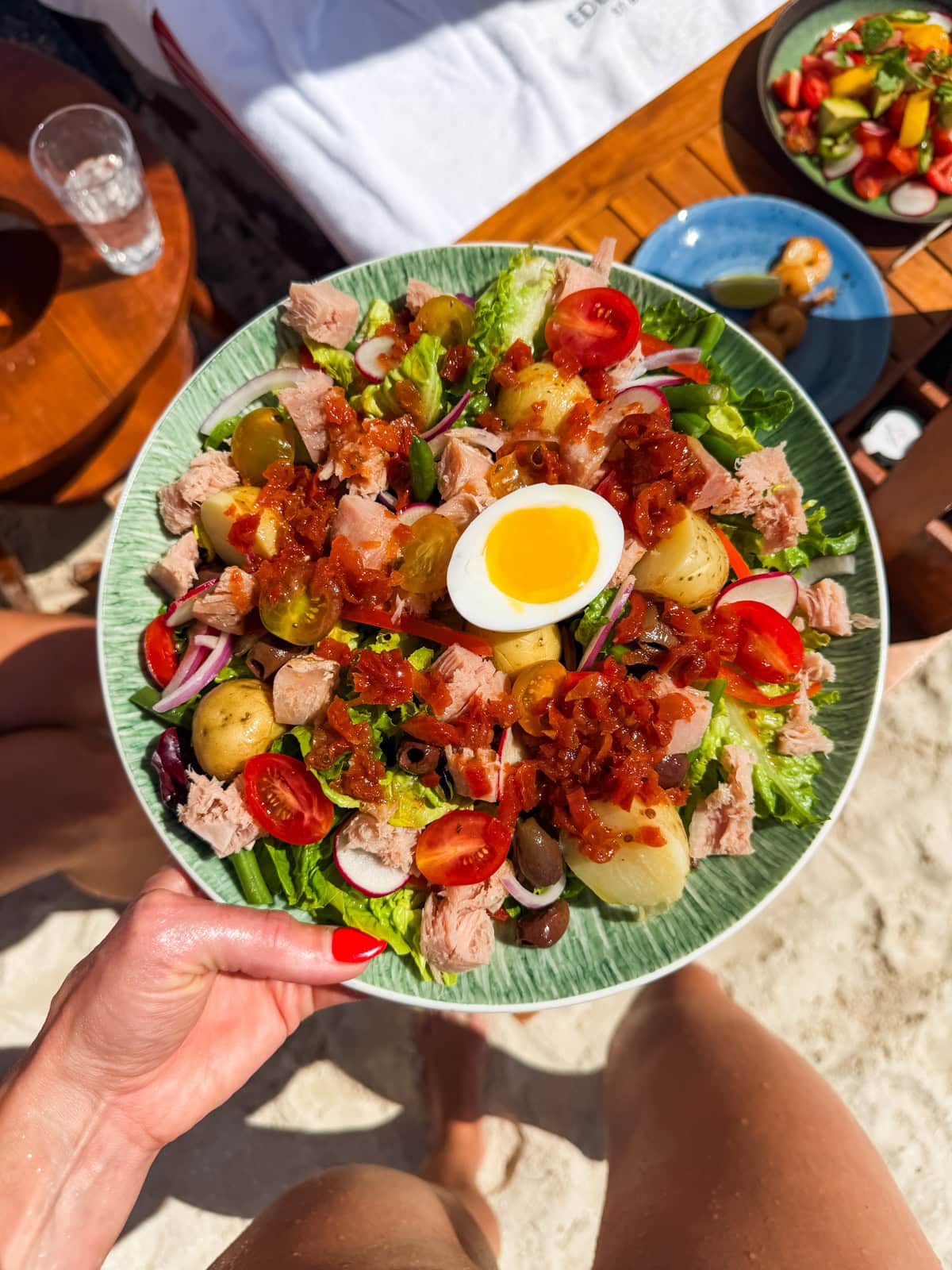 Mango avocado salad with salmon held up at the Sand Bar restaurant, Eden Rock beach in the background