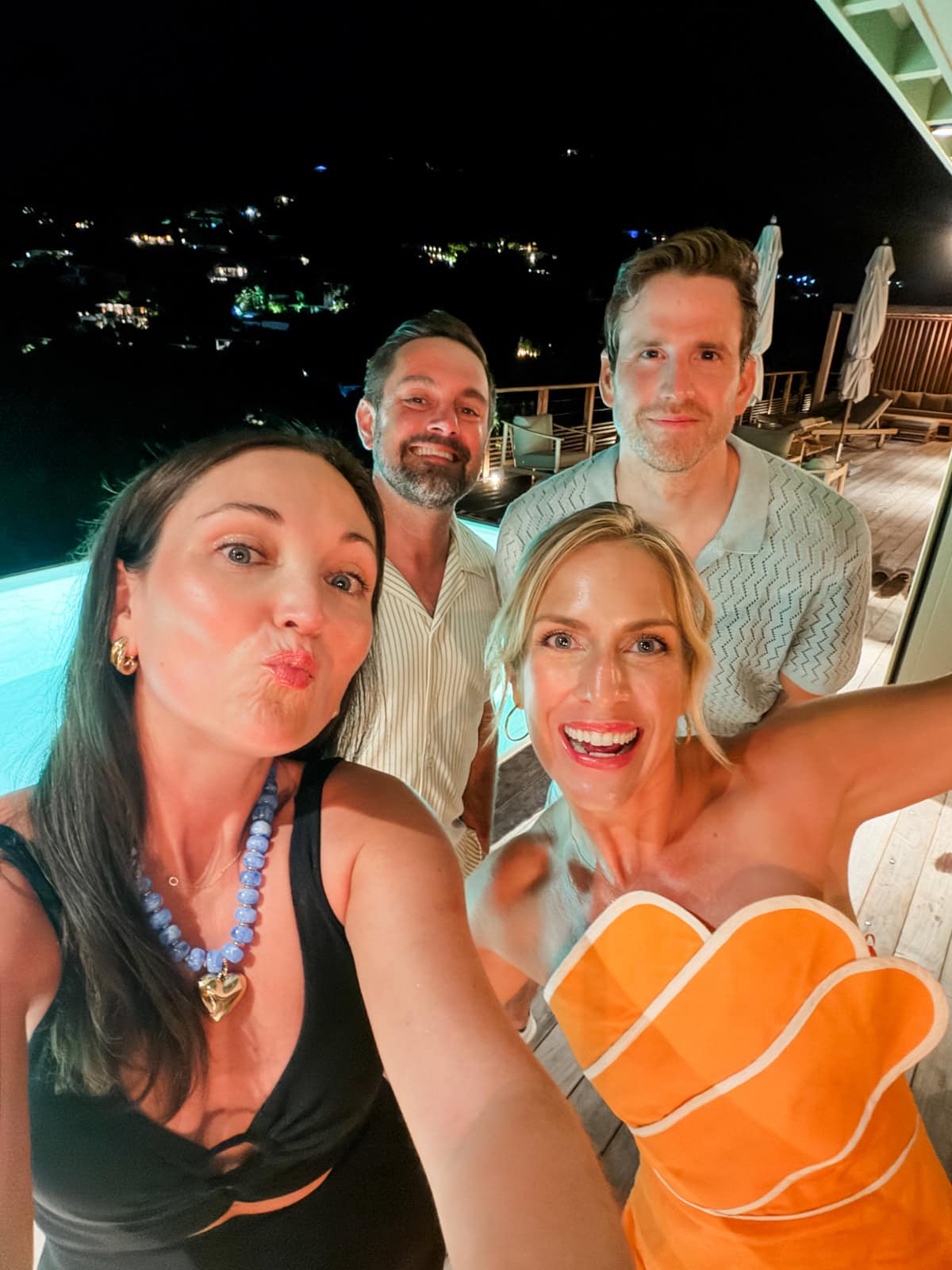 Group of four friends by the villa infinity pool at night with island lights behind them