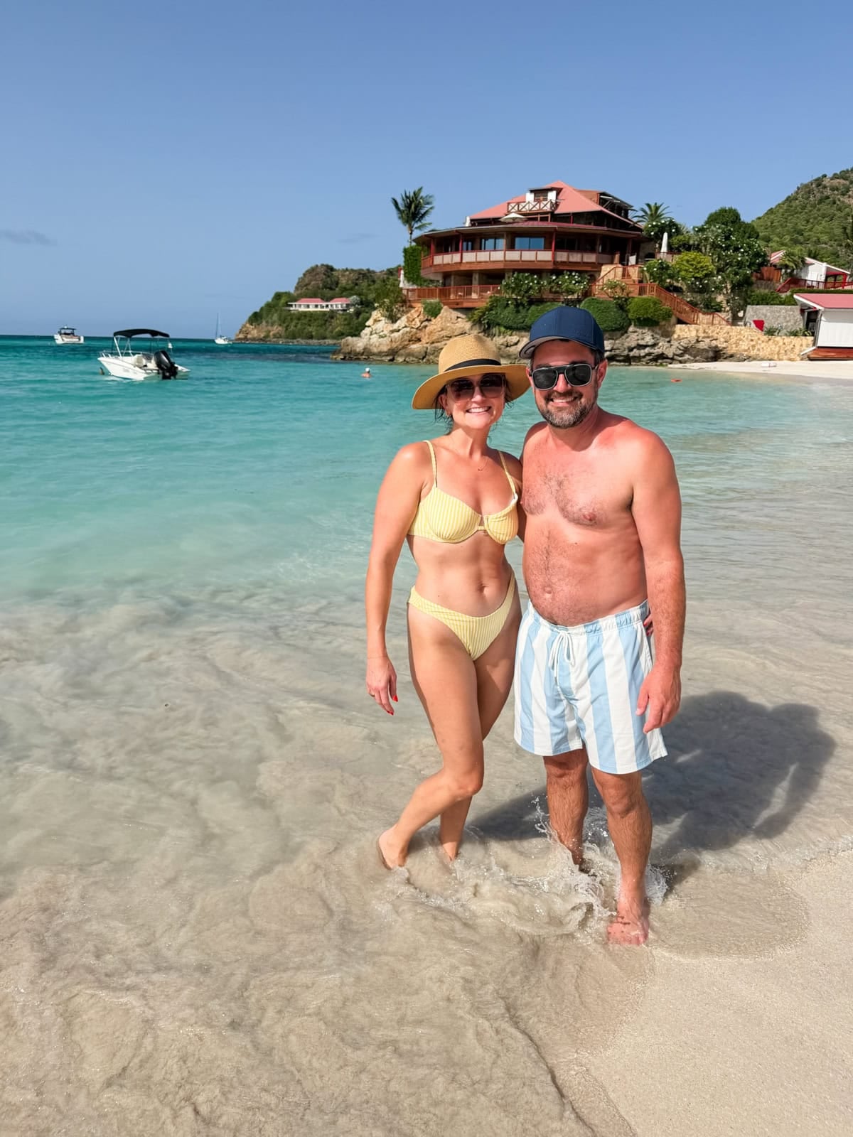 Brittany and Isaac standing in crystal clear turquoise water at St. Jean Beach with Eden Rock in the background