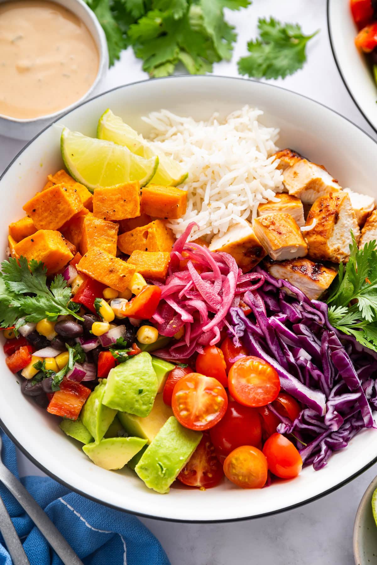 BBQ chicken bowl with white rice, chicken chunks, roasted sweet potatoes, avocado, cherry tomatoes, cabbage, pickled onions and corn and bean salad.
