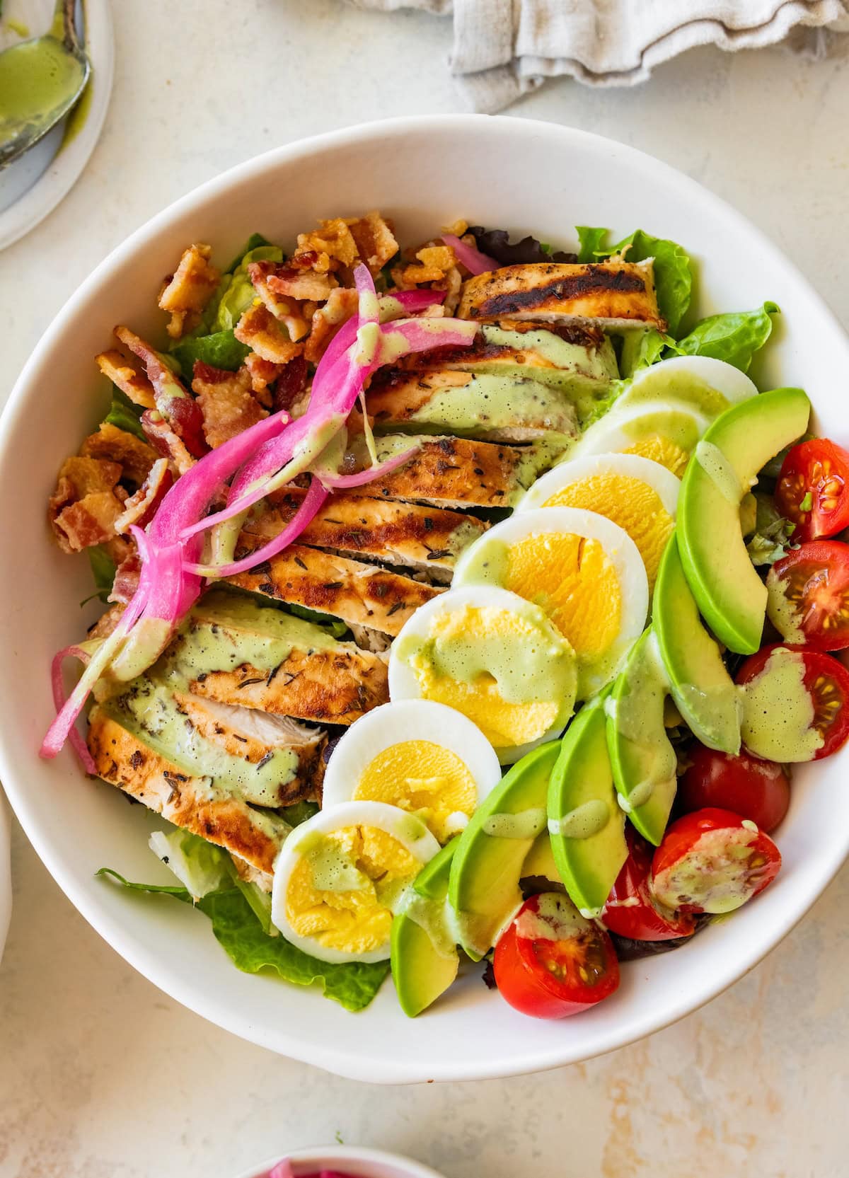 A chicken cobb salad with hard boiled egg, avocado, tomatoes, bacon, and onion in a bowl.