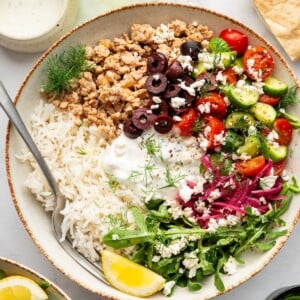 A ground turkey Greek bowl with rice, fresh vegetables, and a lemon wedge.