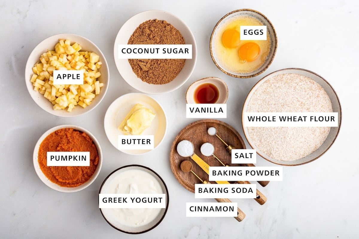 Ingredients measured out to make Healthy Apple Cinnamon Muffins: whole wheat flour, eggs, vanilla, sea salt, baking powder, cinnamon, baking soda, coconut sugar, butter, Greek yogurt, apple and pumpkin.