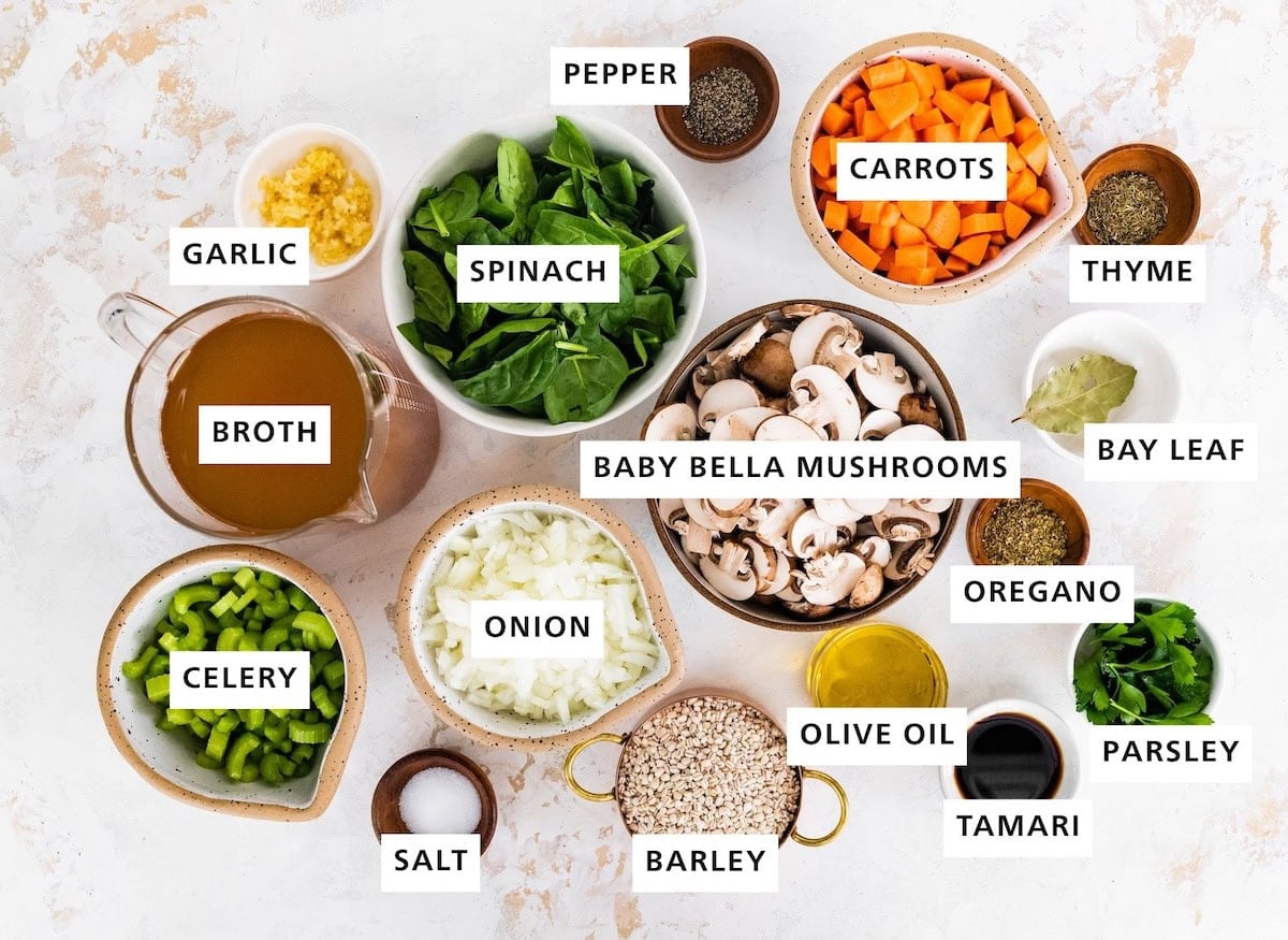 Ingredients measured out to make Mushroom Barley Soup: celery, broth, garlic, salt, onion, spinach, barley, baby bella mushrooms, pepper, olive oil, carrots, tamari, oregano, parsley, bay leaf and thyme.