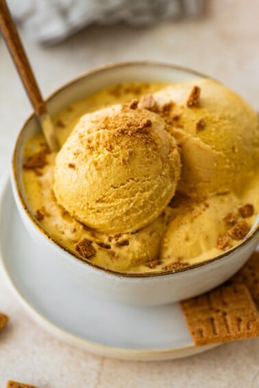 Scoops of cottage cheese pumpkin ice cream in a ceramic bowl topped with crushed graham crackers and served with a spoon.