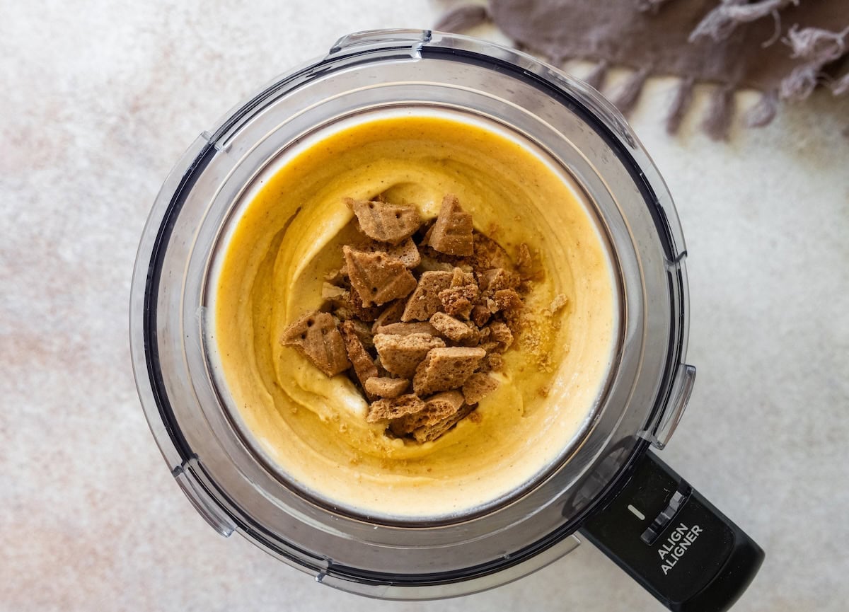 Frozen cottage cheese pumpkin ice cream in the Creami container with crushed graham crackers being mixed in.