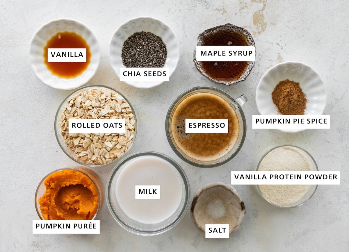 Ingredients measured out for pumpkin spice latte overnight oats: vanilla, chia seeds, maple syrup, pumpkin pie spice, vanilla protein powder, salt, milk, pumpkin puree, rolled oats, and espresso.