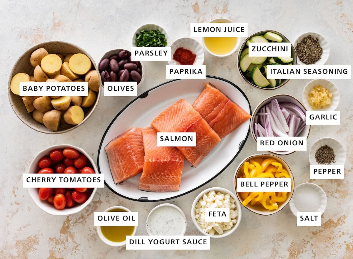 Ingredients measured out for a salmon sheet pan recipe: salmon, red onion, bell pepper, feta, dill yogurt sauce, olive oil, cherry tomatoes, baby potatoes, olives, parsley, paprika, lemon juice, zucchini, Italian seasoning, garlic, pepper, and salt.