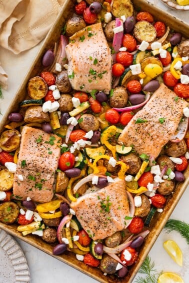A salmon sheet pan meal on a sheet pan with four salmon filets and roasted veggies.