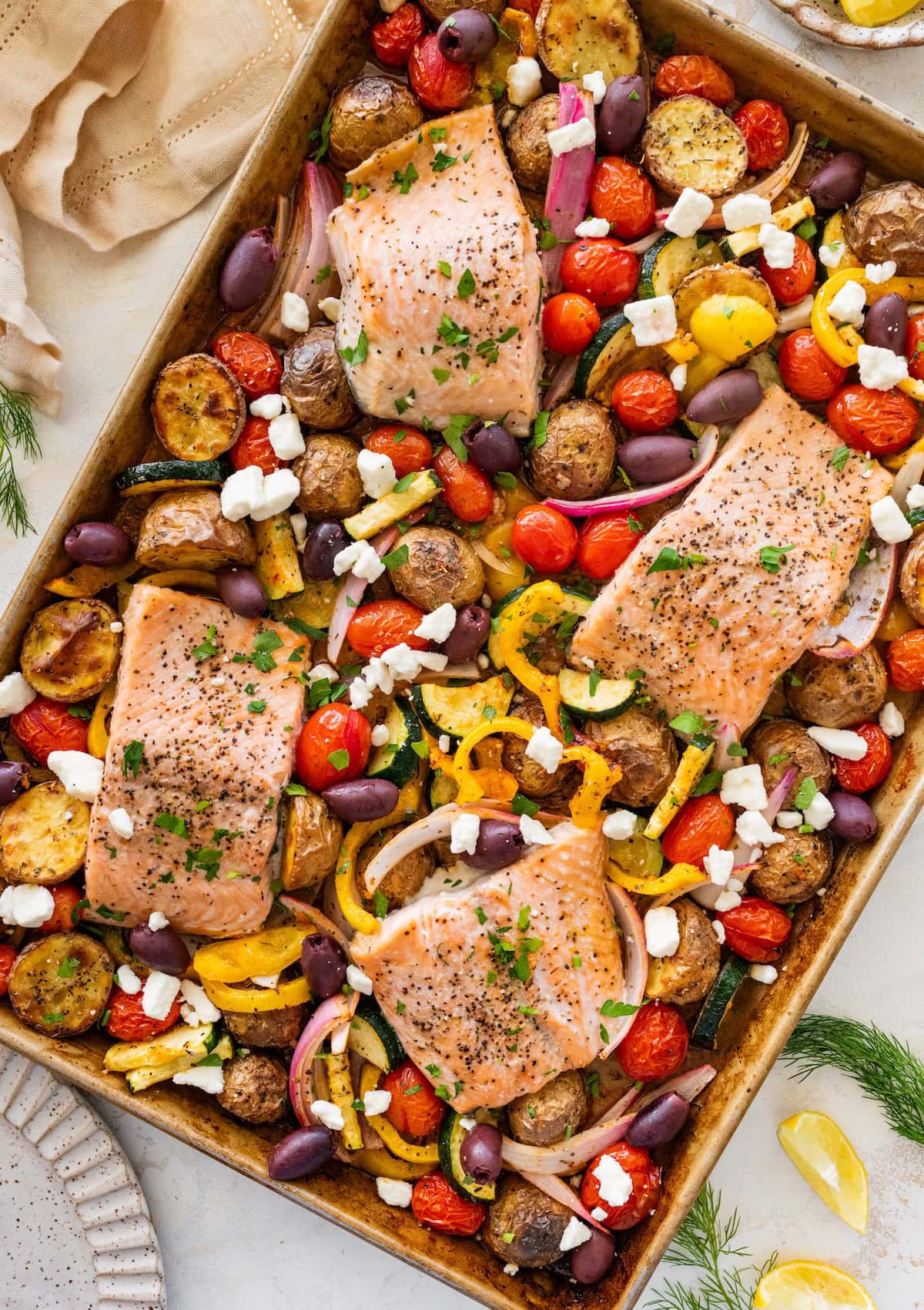 A salmon sheet pan meal on a sheet pan with four salmon filets and roasted veggies.