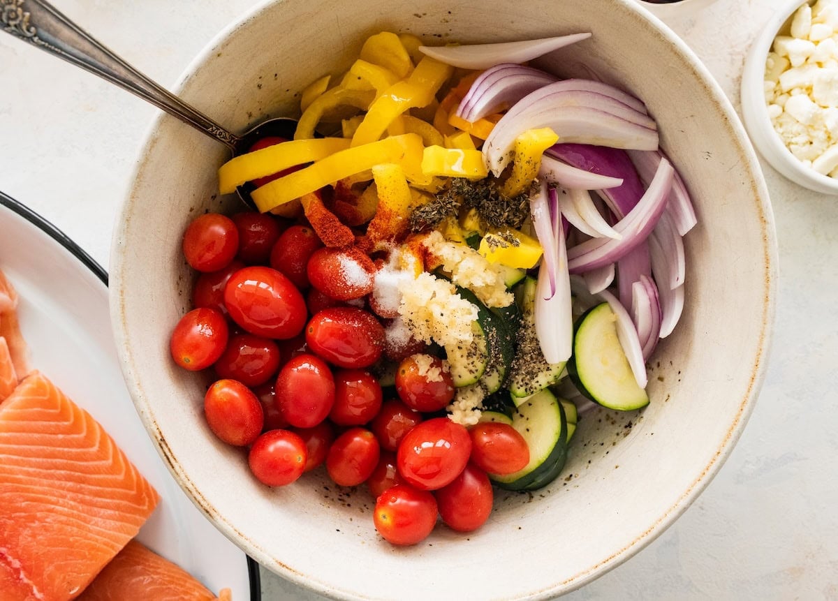 Fresh vegetables in a large mixing bowl with garlic, salt, and pepper.
