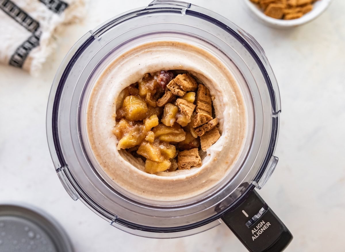 Frozen apple ice cream with cinnamon apples and graham crackers in the middle of it in the Creami container.