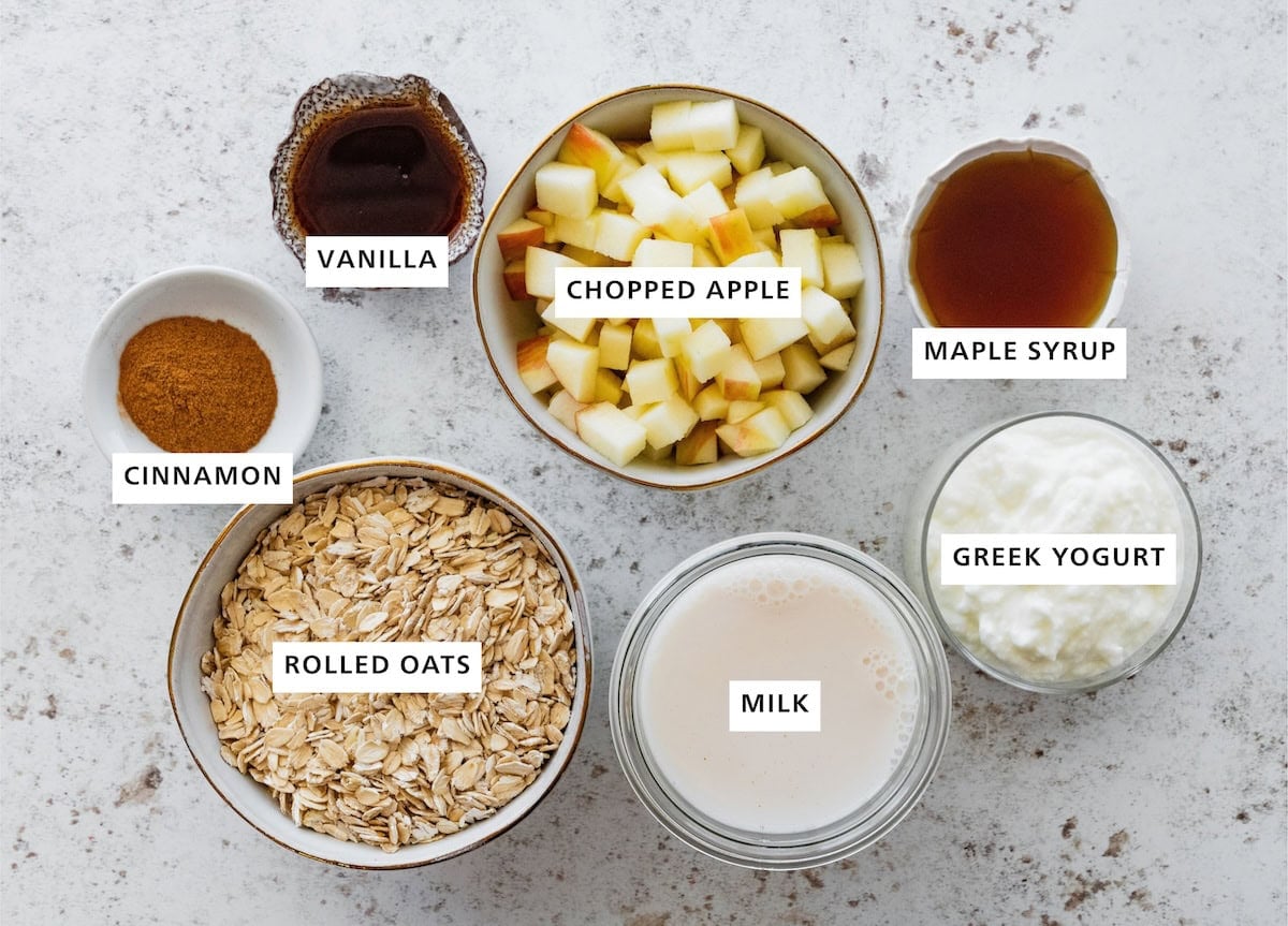 Ingredients measured out for apple pie overnight oats: chopped apple, maple syrup, Greek yogurt, milk, rolled oats, cinnamon, and vanilla.