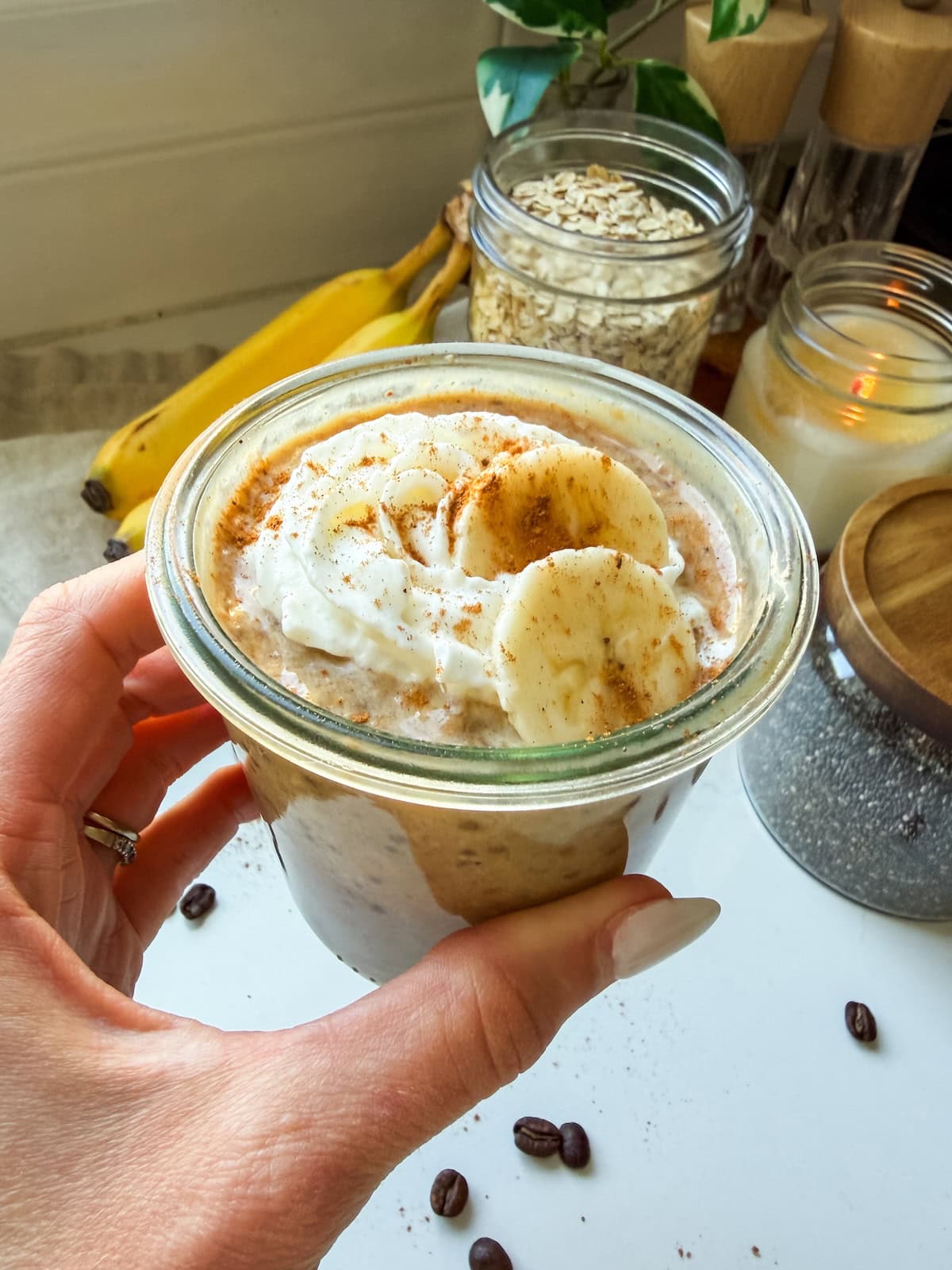 A woman's hand holding a jar of banana bread latte overnight oats.