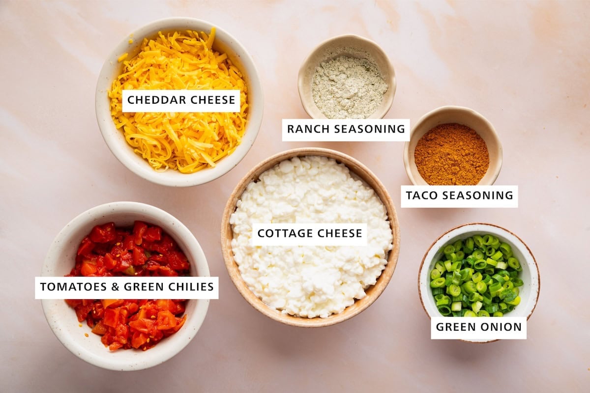 Ingredients measured out for a high-protein boat dip including: cottage cheese, green onion, taco seasoning, ranch seasoning, cheddar cheese, tomatoes, and green chilies.