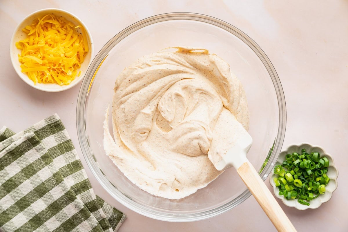 A cottage cheese boat dip being prepared in a large glass bowl with a silicone spatula.