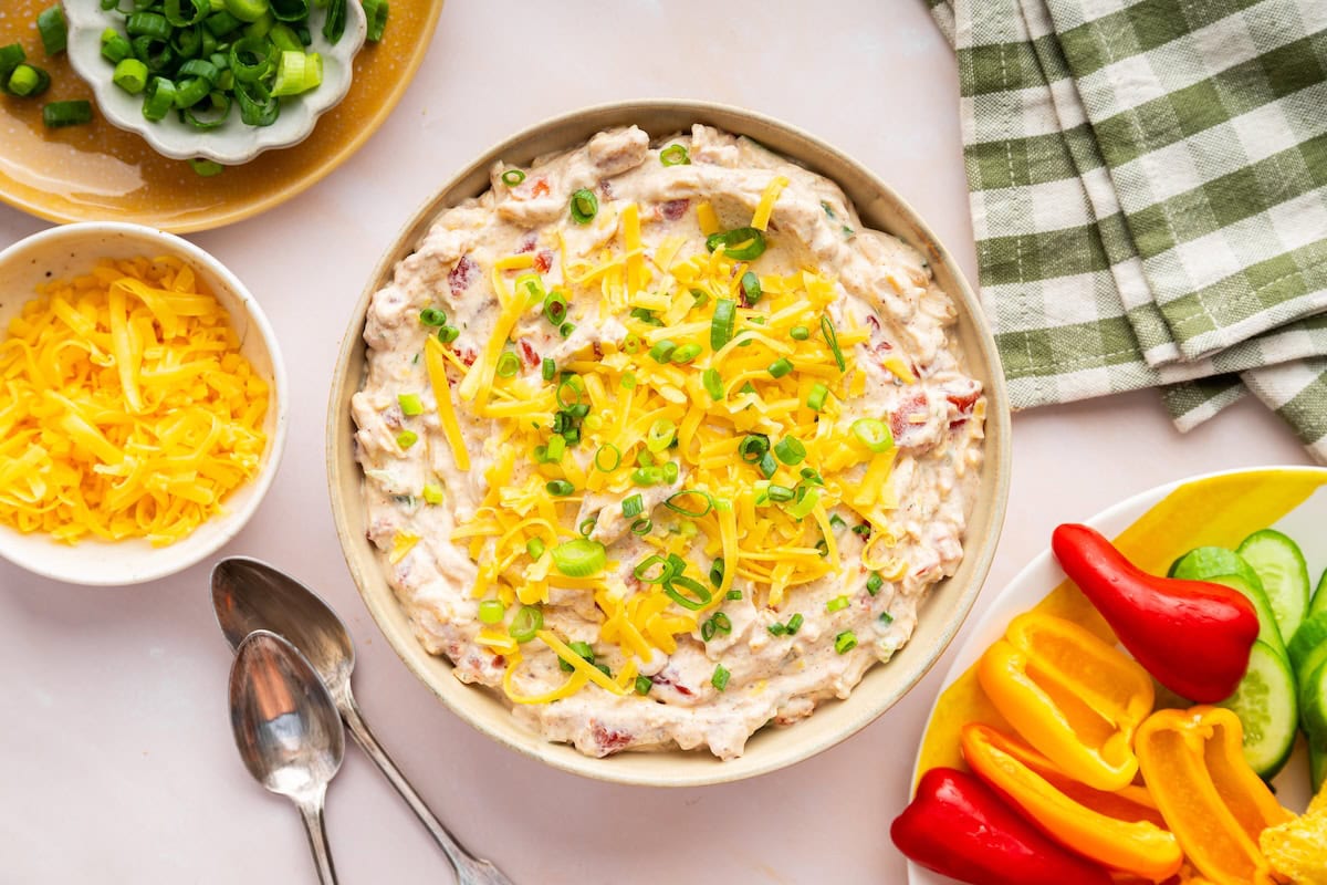 A cottage cheese dip topped with shredded cheese, and green onion in a bowl.