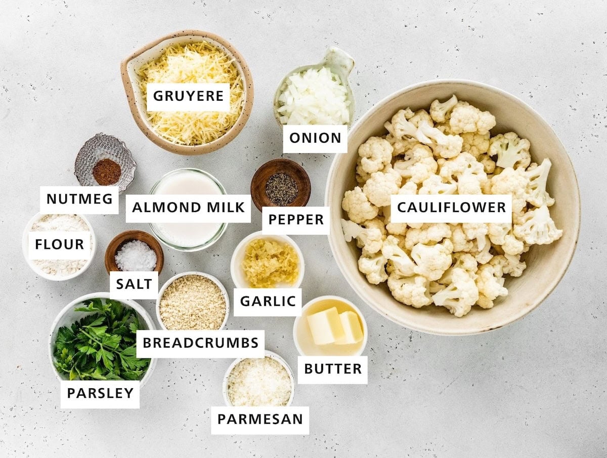 Ingredients measured out to make Cauliflower Gratin: cauliflower, onion, butter, pepper, garlic, parmesan, gruyere, almond milk, panko or almond meal, nutmeg, salt, flour and parsley.