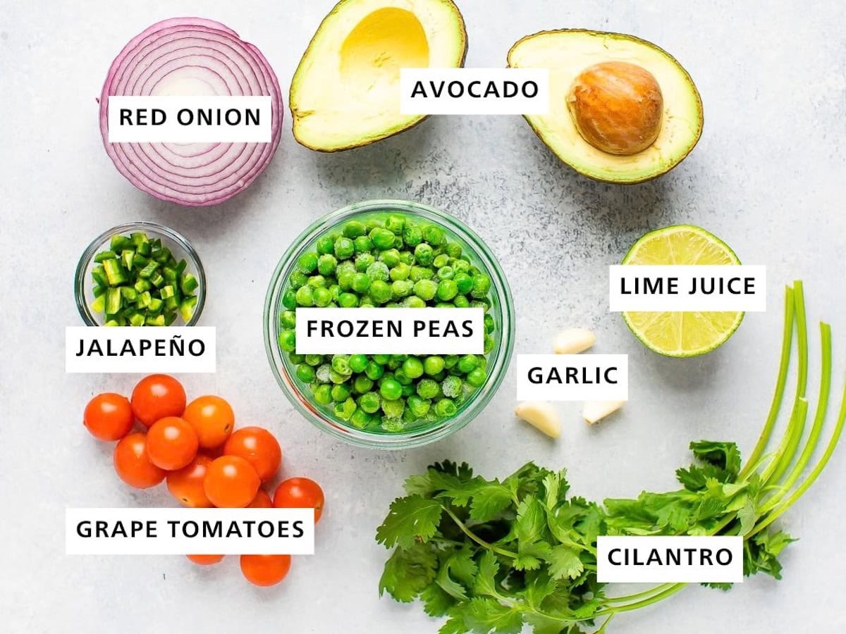 Ingredients measured out for healthy guacamole: frozen peas, avocado, lime juice, garlic, cilantro, grape tomatoes, jalapeño, and red onion.