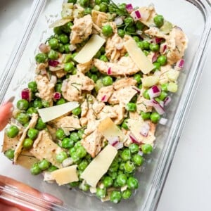 A glass container with peas, chicken and shaved parm (the viral chicken and peas salad).