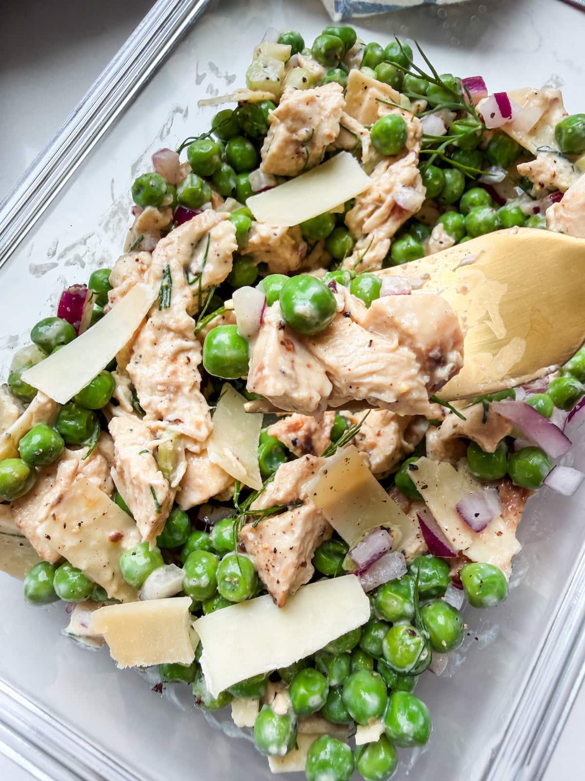 A glass container with peas, chicken and shaved parm (the viral chicken and peas dish) with a gold fork bite.
