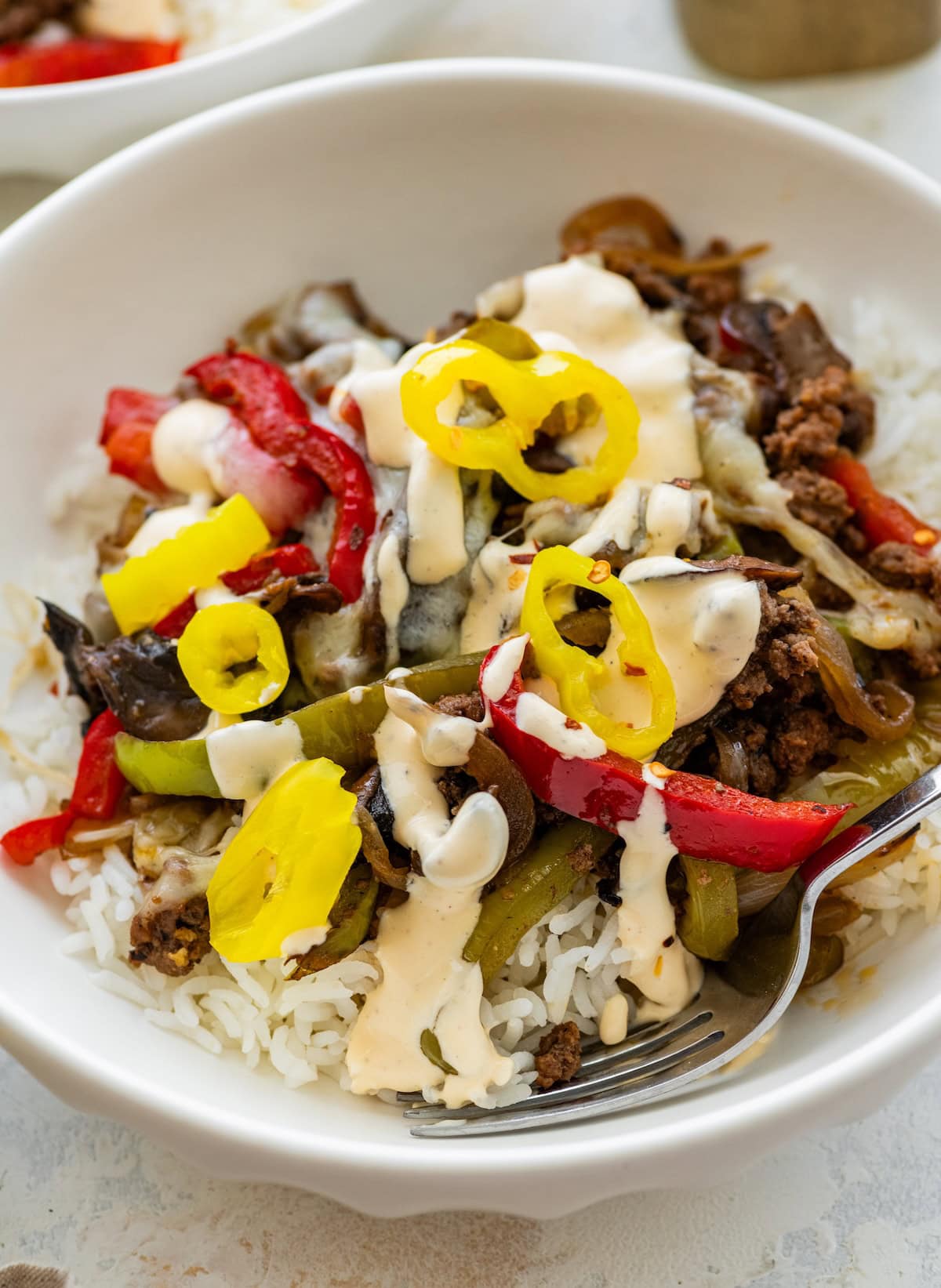 Ground beef philly cheesesteak bowls served over white rice topped with banana peppers and a cheese sauce.