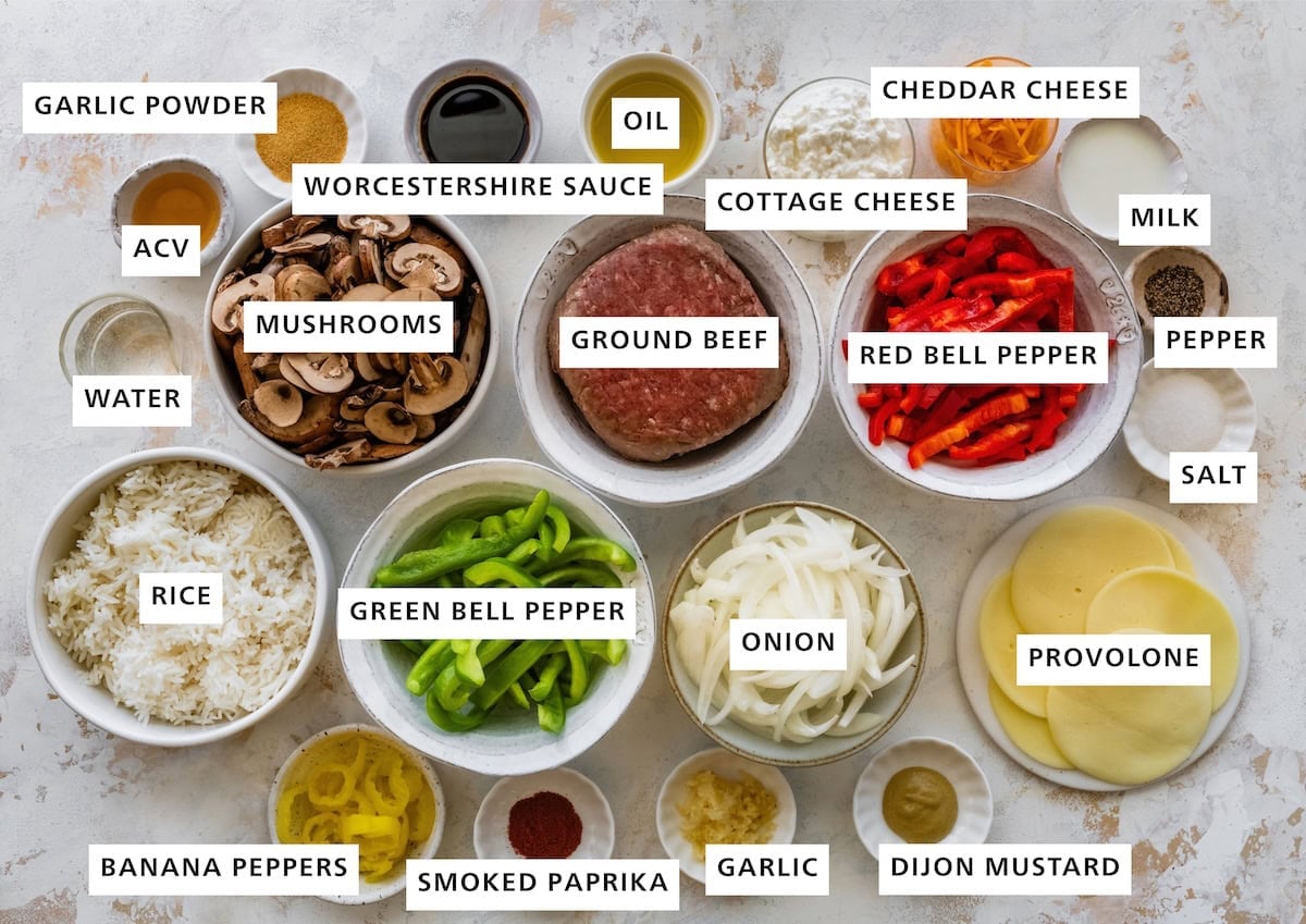 Ingredients for Philly cheesesteak bowls arranged in bowls, including ground beef, peppers, mushrooms, cheese and seasonings.