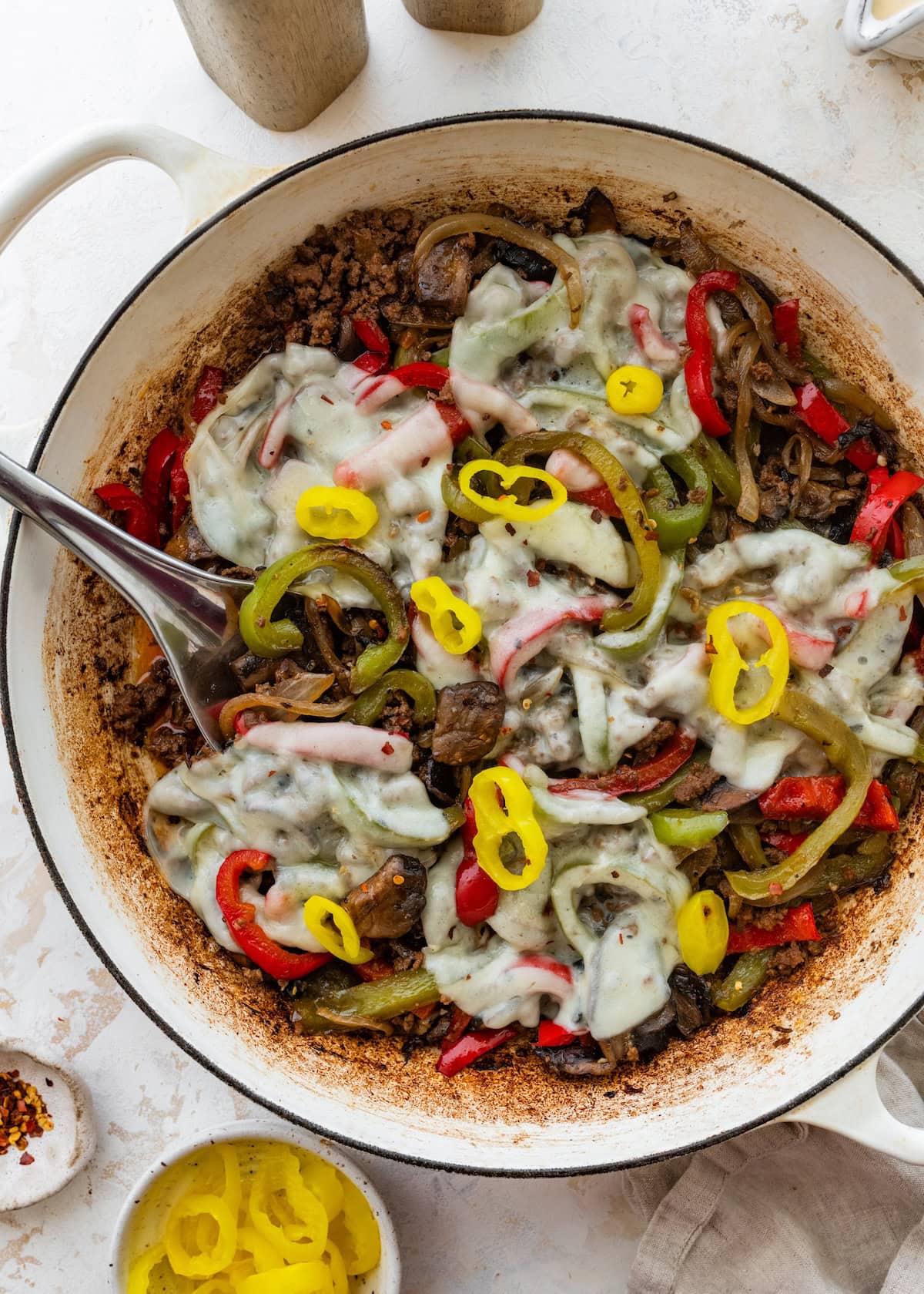 Ground beef and pepper mixture in a skillet topped with melted provolone cheese and banana peppers.