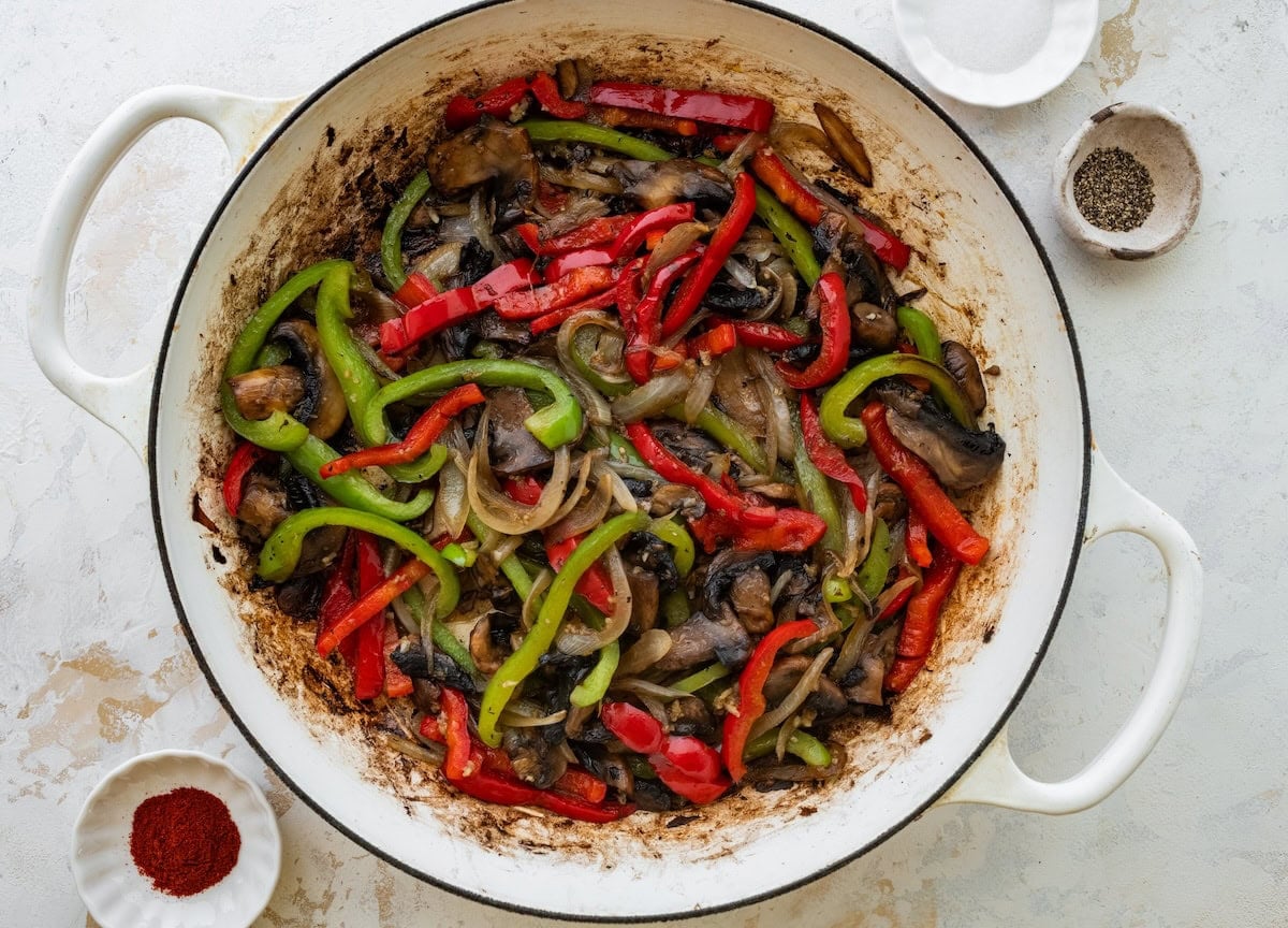 Sliced peppers, onions and mushrooms sautéing in a skillet.