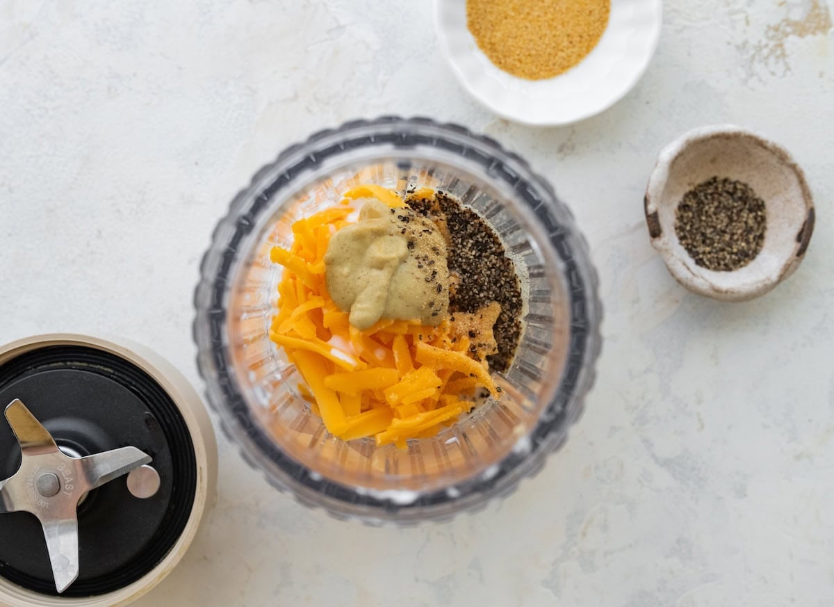 Cottage cheese, shredded cheddar and seasonings in a blender bowl for cheese sauce.