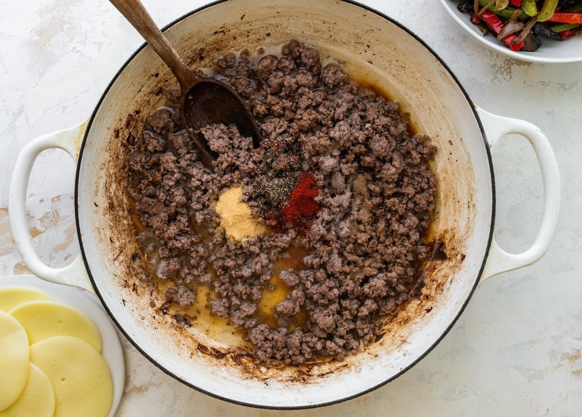 Seasoned ground beef cooking in a skillet with seasonings.