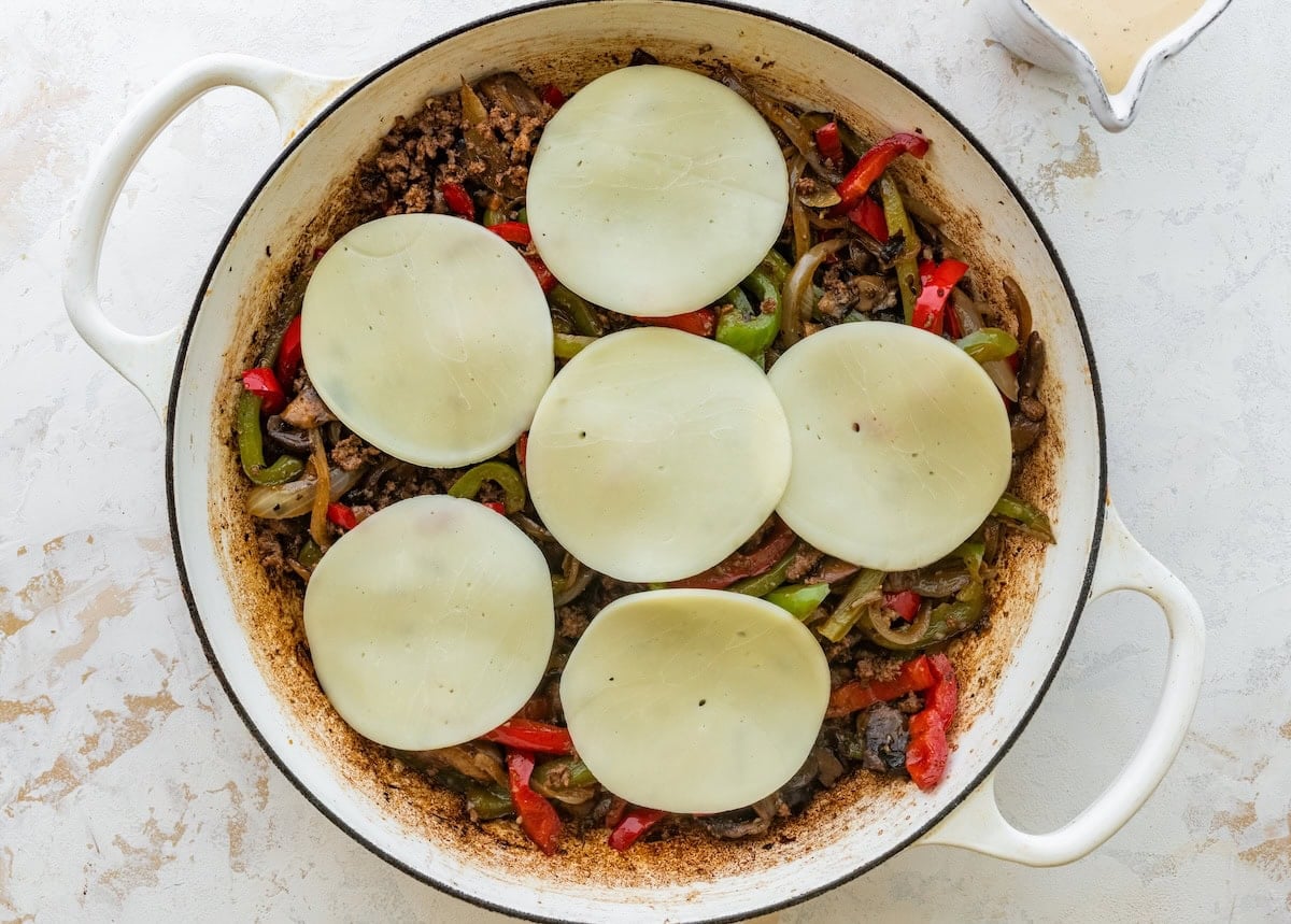Provolone slices melting over ground beef, peppers and onions in a skillet.