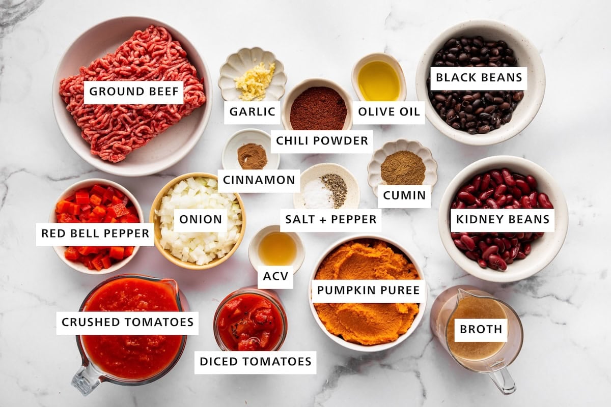 Ingredients for pumpkin chili arranged in small bowls, including ground beef, beans, pumpkin, tomatoes, vegetables and spices.