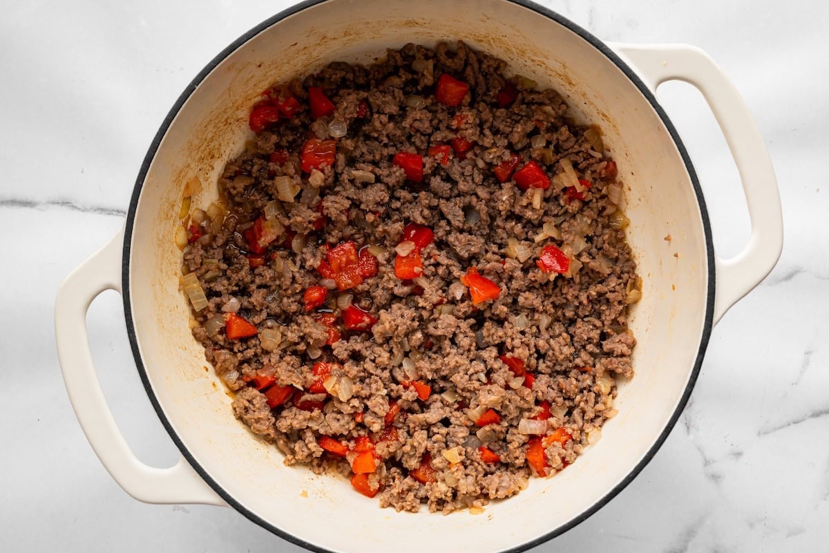 Ground meat cooking with onion and red bell pepper in a Dutch oven.